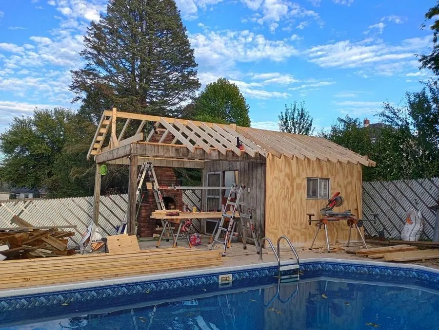 Pool house and cabana under construction beside in-ground pool, framing and sheathing stage