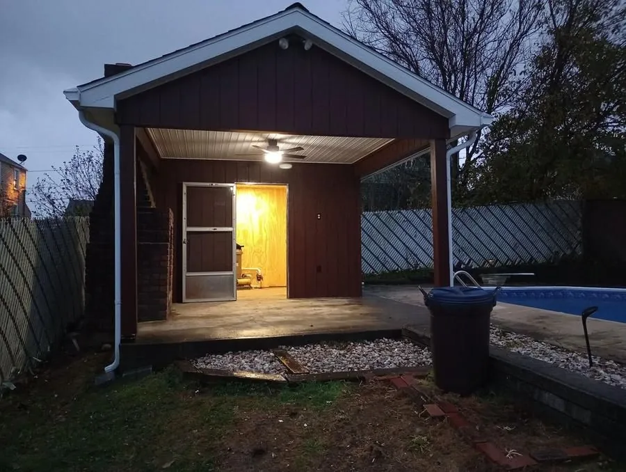 Completed pool house with covered porch, ceiling fan, and exterior lighting beside pool