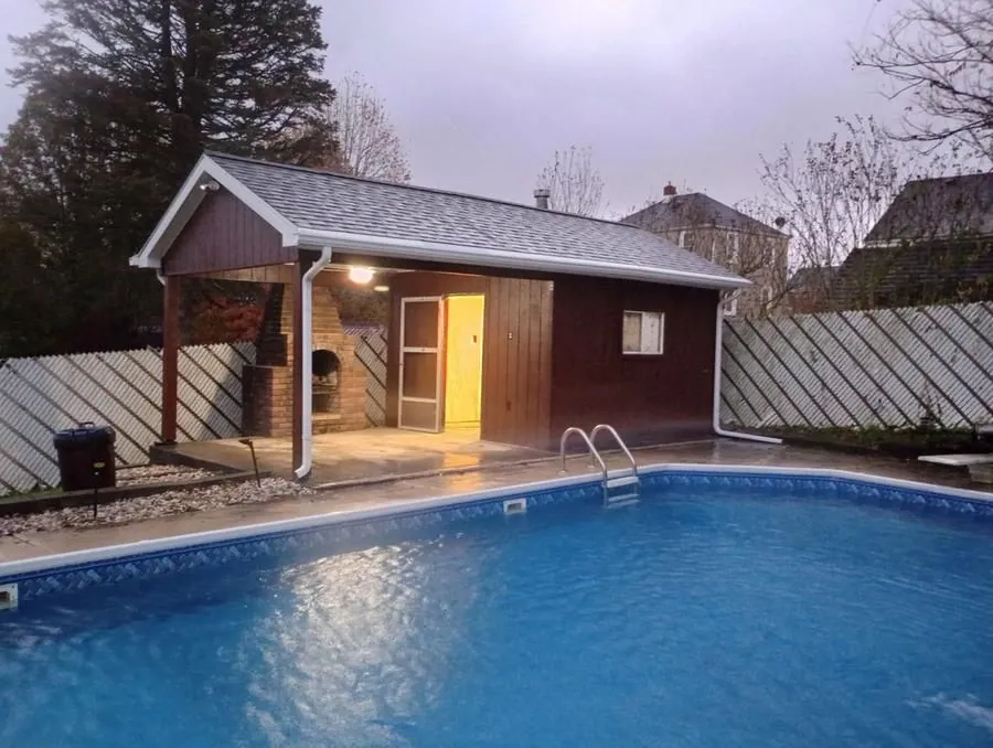 Pool house with covered porch, brick outdoor fireplace, and in-ground pool, wide view